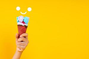 Close up hand holding colorful ice cream cone on yellow background photo