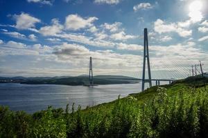 Seascape of green field by Golden Horn Bay and the Zolotoy Bridge with cloudy blue sky in Vladivostok, Russia photo