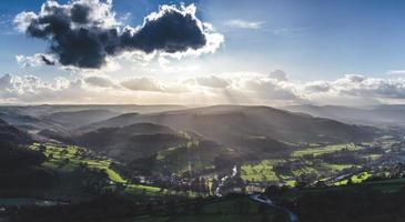 Aerial view of trees and hills with low sun in cloudy blue sky photo