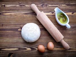 Raw pizza dough and rolling pin with eggs on a wooden background