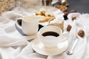 Cup of coffee, saucer, and cream server next to pastries on rumpled tablecloth photo