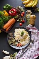 Pasta carbonara with bacon and parmesan, lettuce, and sliced tomatoes on a black dish photo