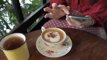 Latte Art Kaffee auf dem Tisch, Frau mit Smartphone