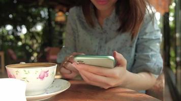 Primer plano de una mujer asiática tomando un café y usando un teléfono inteligente video
