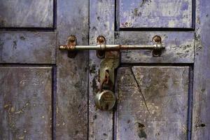 Locked padlock with a chain on a violet wooden door of an old building photo