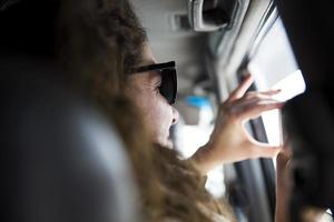 Young woman taking a photo with mobile phone from inside a vehicle on a road trip