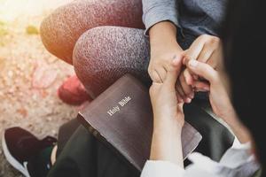 dos mujeres tomados de la mano y orando mientras estudian la biblia foto