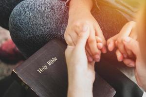 Two women holding hands and praying as they study the bible photo