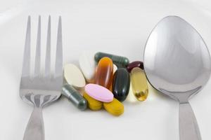 Multiple drug pills on a plate with a spoon and fork photo