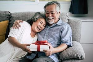 Elderly couple surprises with gift box in living room photo