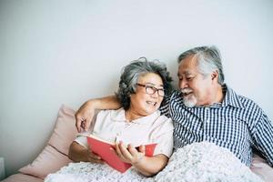 pareja de ancianos acostada en la cama y leyendo un libro