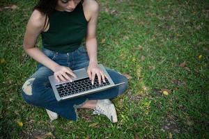 Young beautiful woman sitting on green grass and using laptop in the park photo