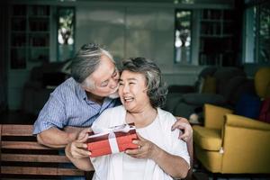 Smiling senior husband making surprise giving gift box to his wife photo