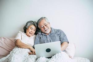 pareja de ancianos hablando y usando la computadora portátil en el dormitorio foto
