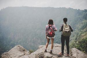 Pareja de excursionistas con mochilas de pie en la cima de una montaña y disfrutando de la vista de la naturaleza foto