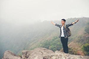 Hiker with backpack standing on top of a mountain with raised hands photo