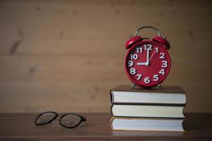 Alarm clock at 9am on stack of books with glasses on wooden table photo