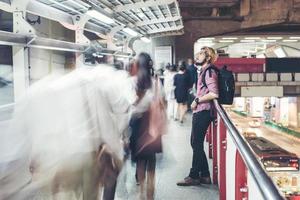 Hombre barbudo hipster de pie en la estación de tren con fondo de movimiento de personas foto