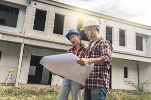 Two workers with hard hats looking at a blue print photo