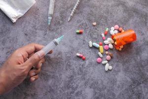 Hand holding syringe with pills on table photo