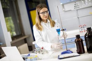 Young female researcher working with blue liquid at separatory funnel photo