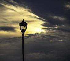 A lamppost silhouetted at sunrise in a cloudy sky photo