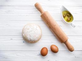 Raw pizza dough and a rolling pin on a wooden background