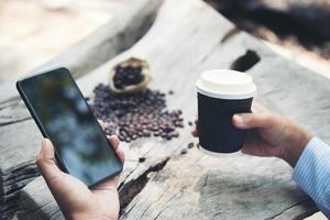 Man hand holding paper cup of coffee with smartphone sitting at wooden table photo