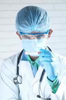 Doctor en mascarilla y vestimenta quirúrgica mirando el tubo rojo foto