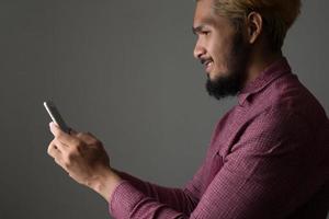 Handsome hipster man smiling while using smartphone isolated on black background photo