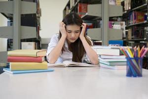 Retrato de estudiante tocando la cabeza mientras lee un libro en la biblioteca de la universidad foto