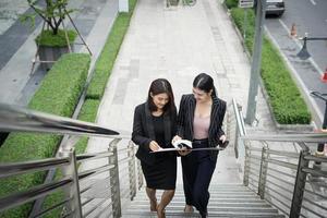 Young Asian business women with documents walking on stairs photo