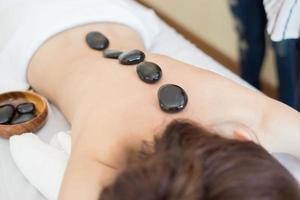 Hermosa joven recibiendo masaje con piedras calientes en el salón spa foto