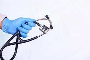 La mano del médico en guantes protectores sosteniendo estetoscopio aislado sobre fondo blanco. foto