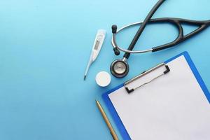 Stethoscope, thermometer, and clipboard on blue background photo