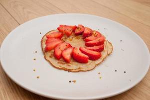 Strawberry pancake on a white plate on a wooden table photo