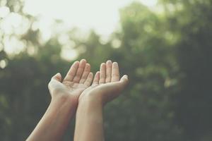 Hands placed together like praying in front of nature green background photo