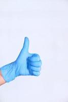 Thumbs up vistiendo guante azul sobre fondo blanco. foto