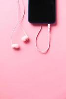 teléfono inteligente y auriculares sobre fondo rosa foto