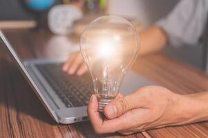 A man holding a light bulb gear symbol while using a computer photo