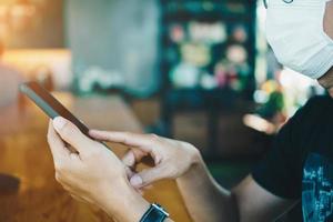 Man wearing a mask using a smartphone in public cafe photo