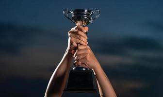 A man holding up a trophy cup on against cloudy twilight sky background photo