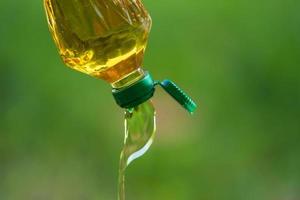 Vegetable oil pouring from bottle with nature background photo