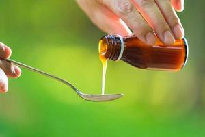 Mano de hombre vertiendo medicación o jarabe antipirético de botella a cuchara con fondo de naturaleza foto