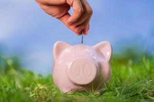Pink piggy bank on grass with hand putting in a coin photo