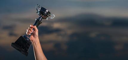 A man holding up a trophy cup on against cloudy twilight sky background photo