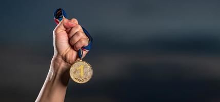 Hand holding gold medal on against cloudy twilight sky background
