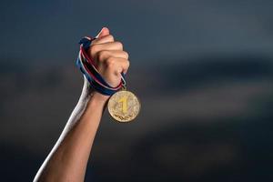 Hand holding gold medal on against cloudy twilight sky background photo