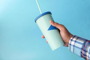 sosteniendo la taza de café ecológica reutilizable sobre fondo azul foto