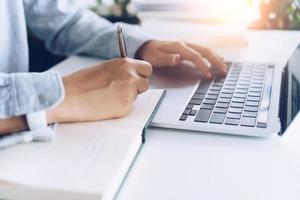 Woman writing in a planner notebook while using laptop at home photo